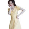 Model wearing yellow bellflower a-line dress with ruffle collar and button front in marble bathroom setting